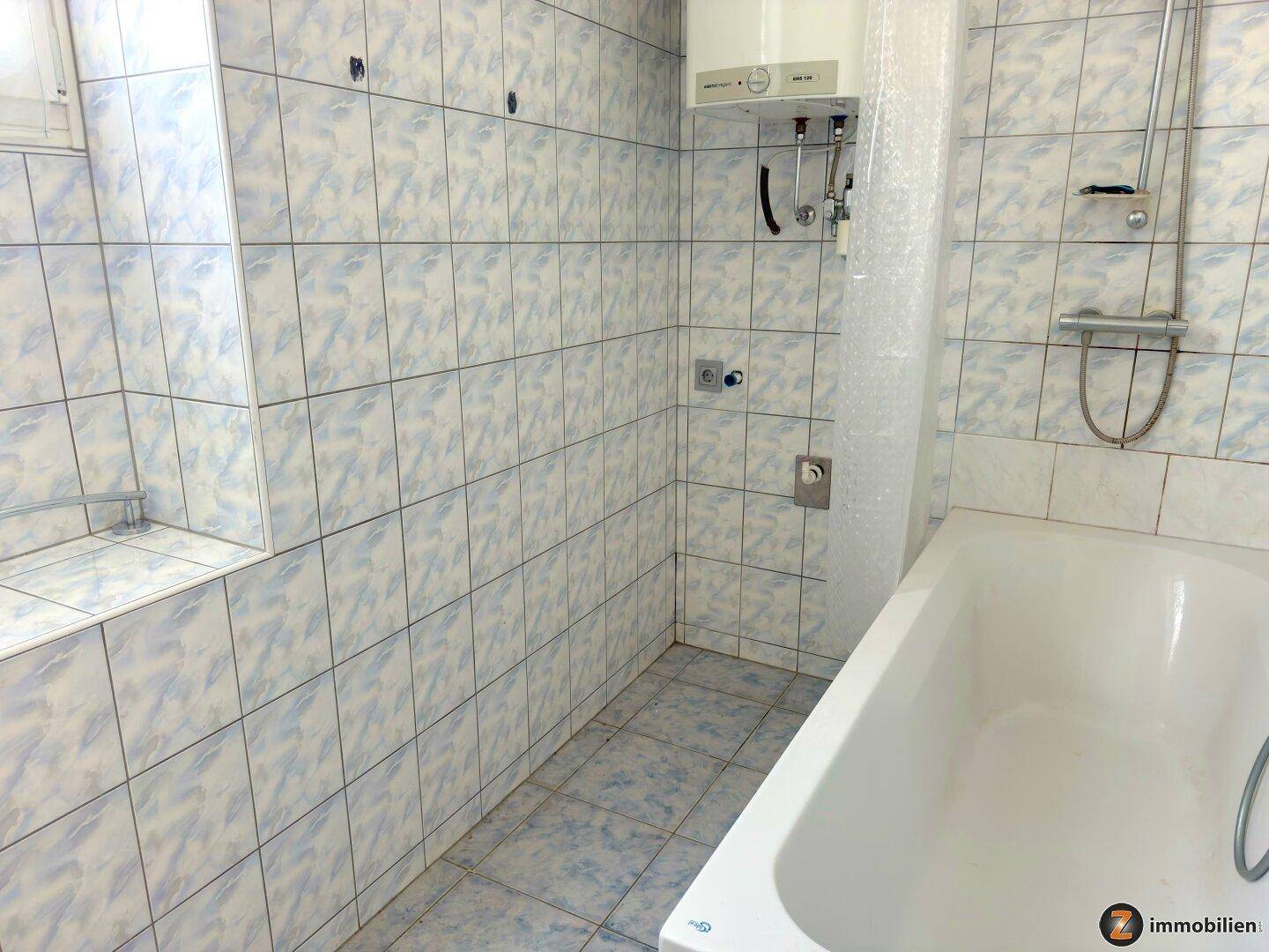 Badezimmer mit Badewanne, Dusche und hellblauen Fliesen an Wänden und Boden.