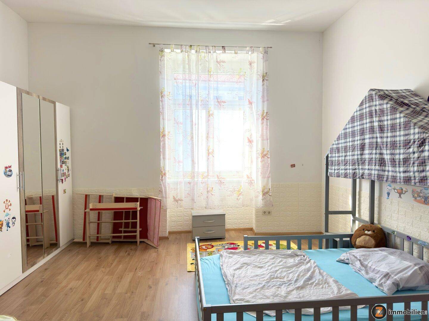 Kinderzimmer mit Etagenbett, Kleiderschrank und hellem Laminatboden.