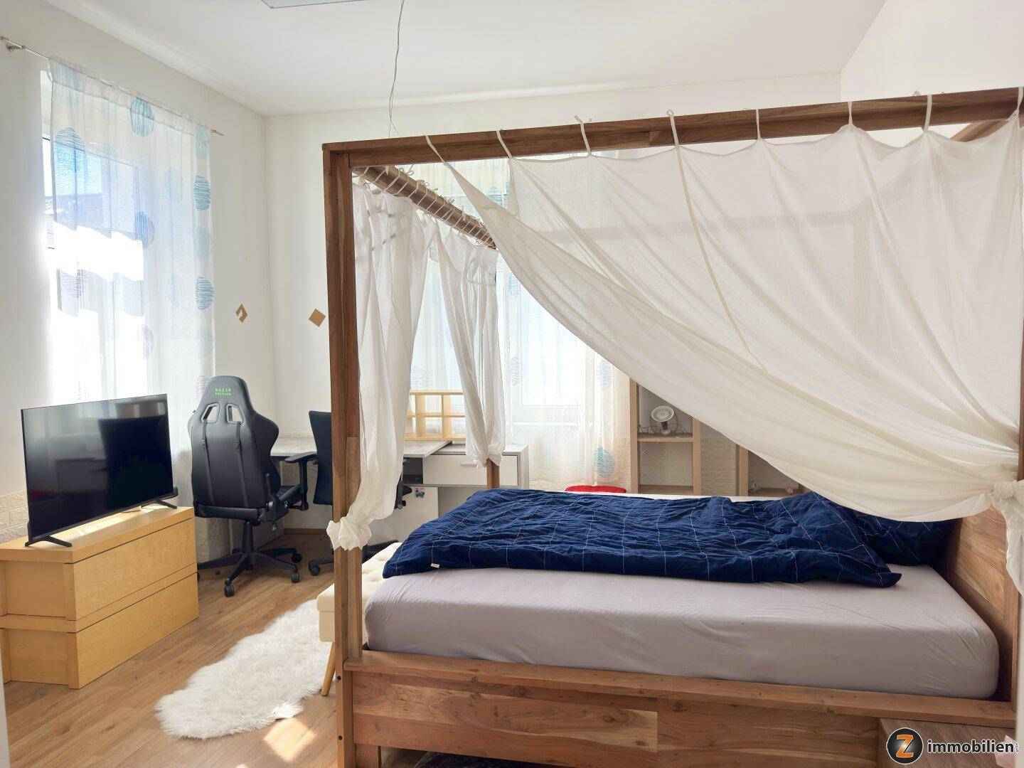 Schlafzimmer mit Himmelbett, Schreibtisch und großem Fenster für viel Tageslicht.