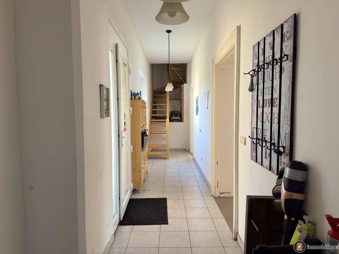 Heller Flur mit Fliesenboden, Garderobe und Treppe zum Obergeschoss.