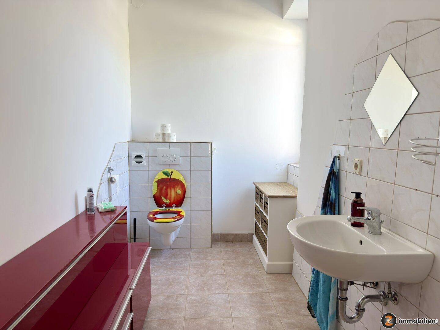 Helles WC mit Waschbecken, Spiegel und farbenfrohem Toilettensitz.
