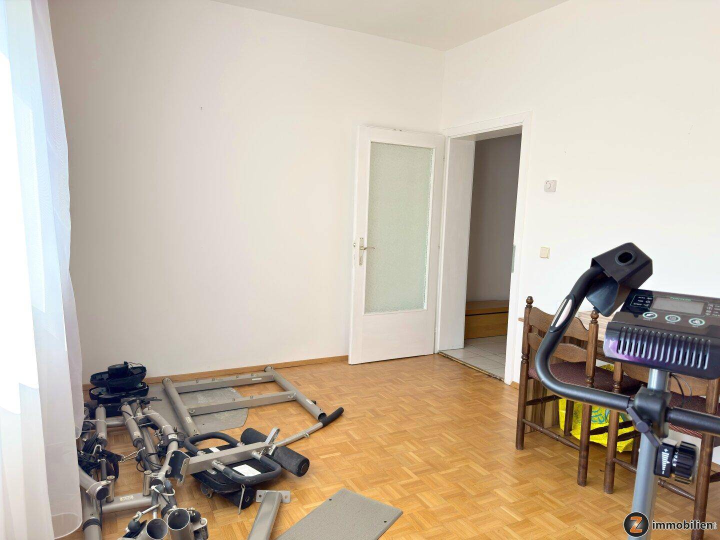 Raum mit Parkettboden und Fitnessgeräten, der vielseitig genutzt werden kann.