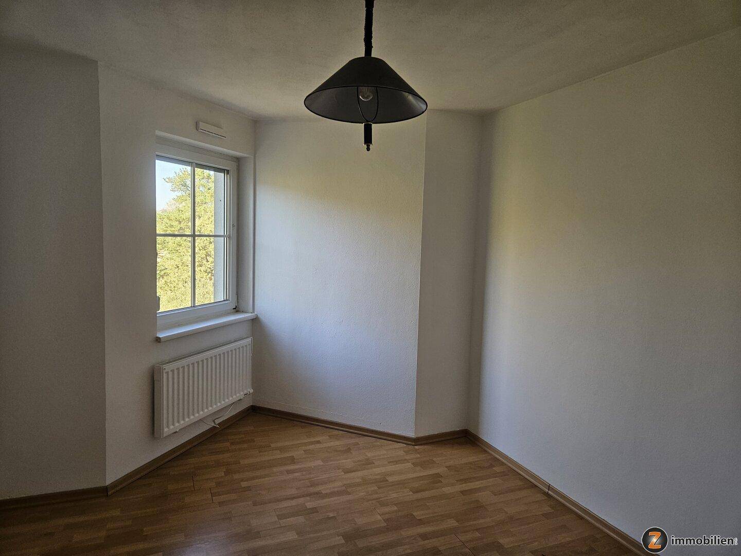 Helles Schlafzimmer mit Parkettboden, Fenster und Heizkörper für angenehme Wärme.