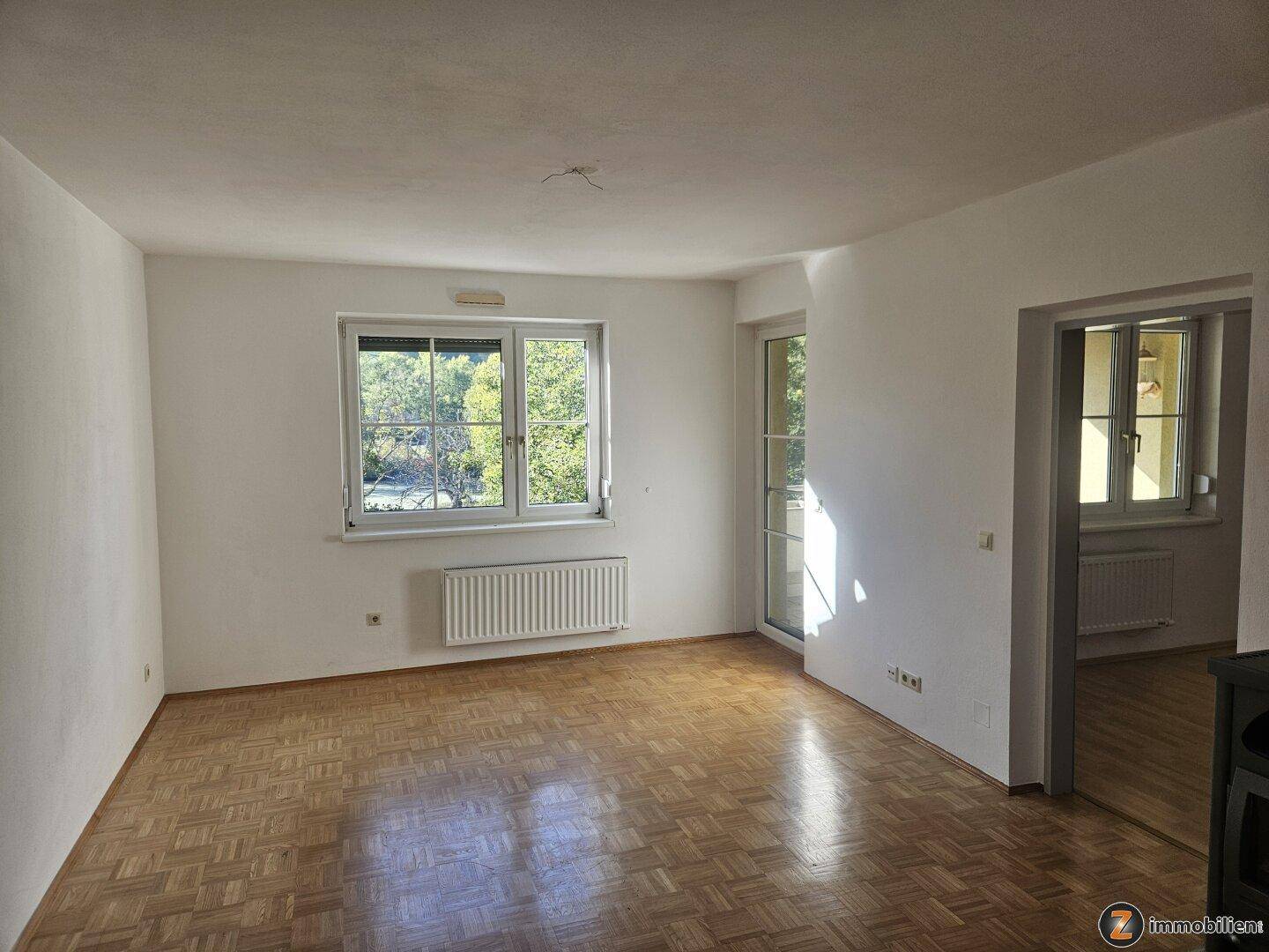 Geräumiges Wohnzimmer mit Parkettboden, großen Fenstern und Zugang zum Balkon.