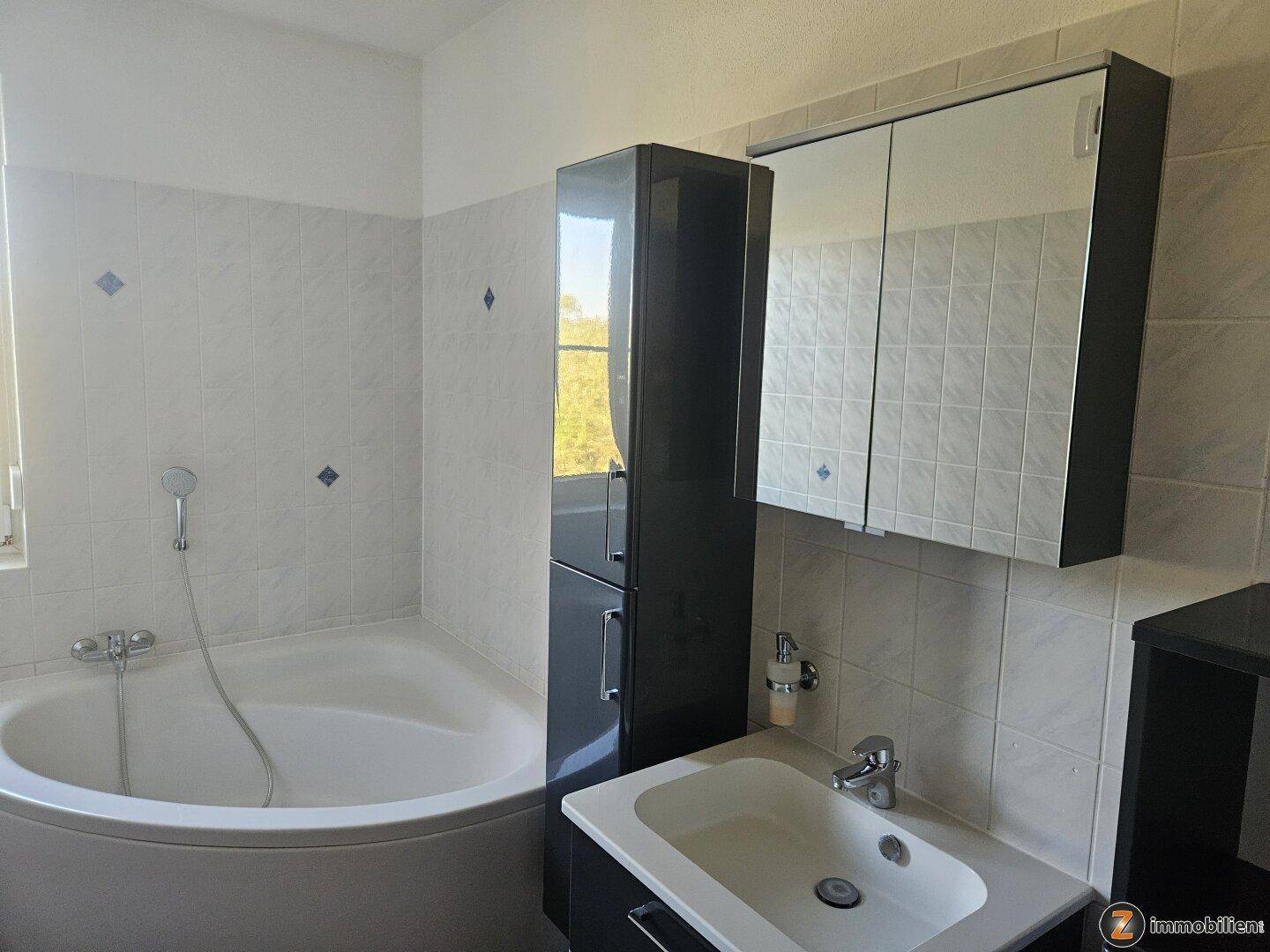 Gefliestes Badezimmer mit Eckbadewanne, Einzelwaschbecken und Spiegelschrank.