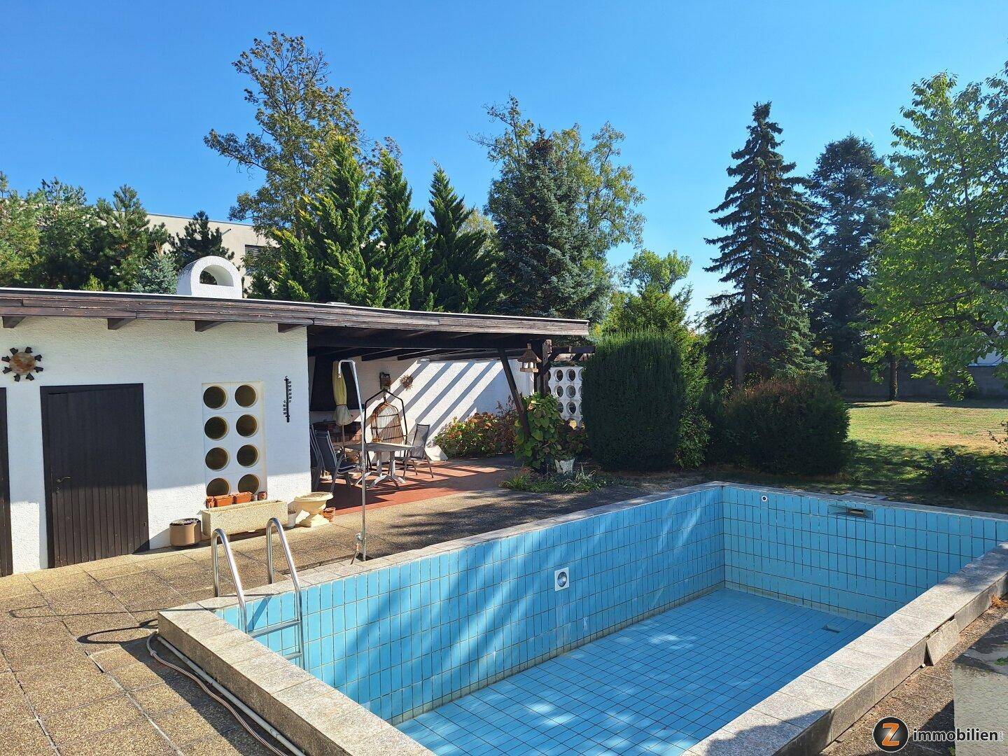 Außenbereich mit Swimmingpool, Poolhaus und überdachtem Sitzbereich im Garten.