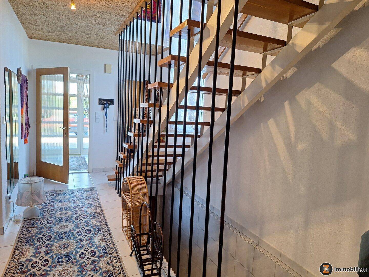 Heller Eingangsbereich mit offener Holztreppe, Fliesenboden und Teppichläufer.