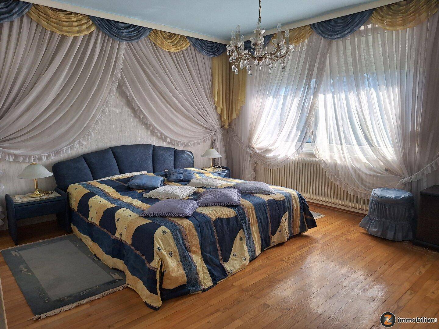 Schlafzimmer mit großem Bett, opulenten Vorhängen und Holzboden.