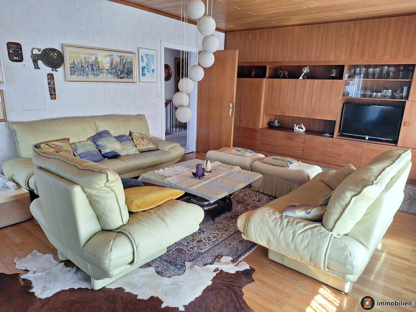Gemütliches Wohnzimmer mit beigen Ledersofas, Holzwänden und Deckenpaneelen.