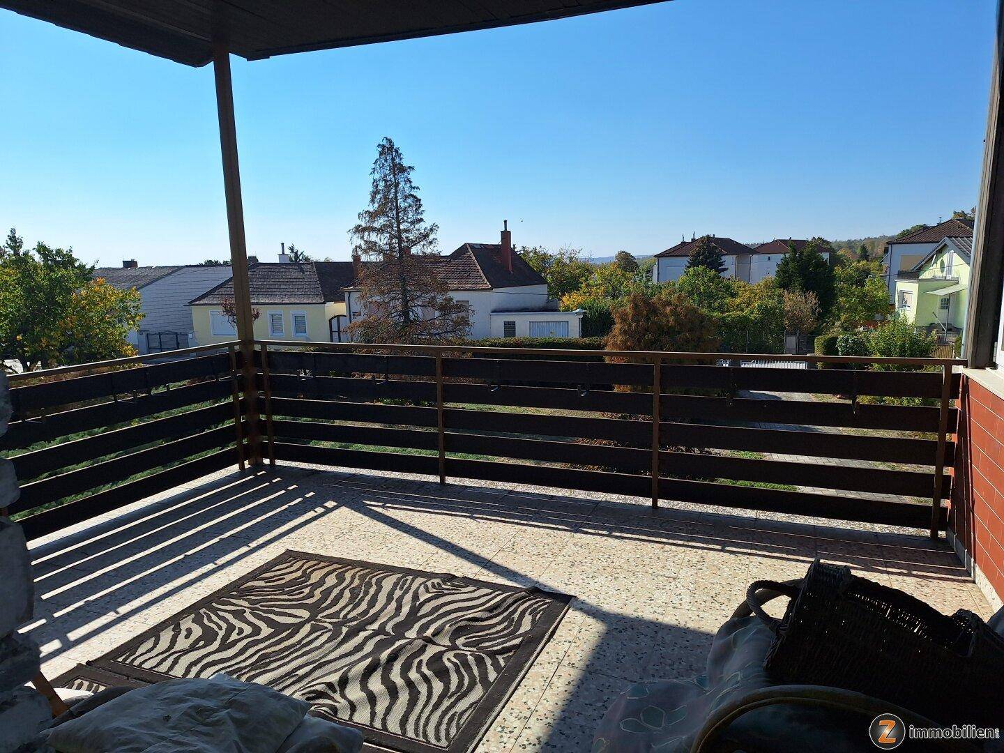 Geräumiger Balkon mit Holzzaun, Teppich und weitem Blick über die Umgebung.