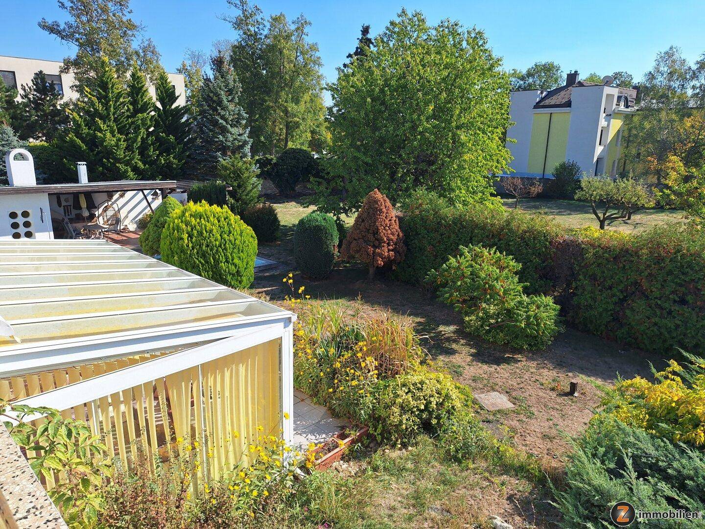 Weitläufiger Gartenbereich mit vielfältiger Bepflanzung und überdachtem Sitzplatz.