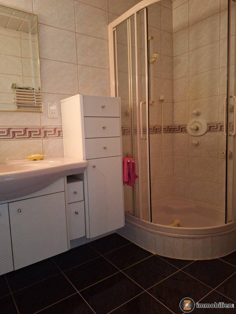 Badezimmer mit Duschkabine, Waschbeckenunterschrank und dunklen Fliesen.