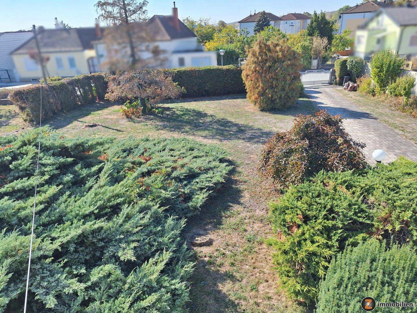 Blick von oben auf den weitläufigen Garten mit verschiedenen Sträuchern und Auffahrt.