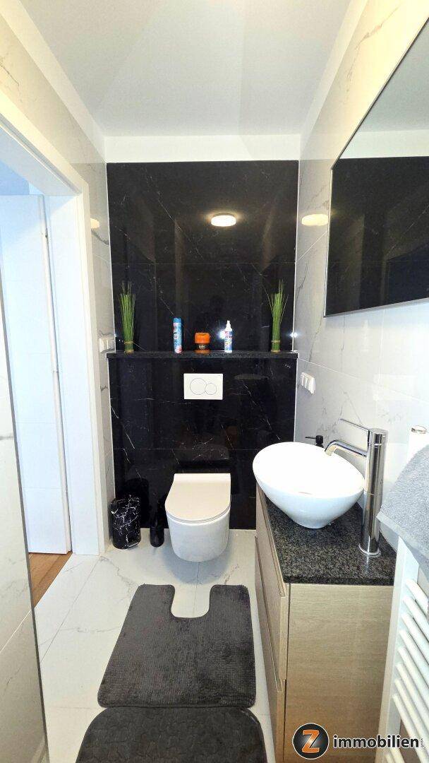Modernes Gäste-WC mit wandhängender Toilette, stilvollem Waschbecken und dunklen Akzentfliesen.