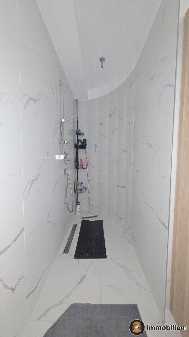 Geräumige begehbare Dusche mit eleganten Marmoroptik-Fliesen und Regenduschkopf.