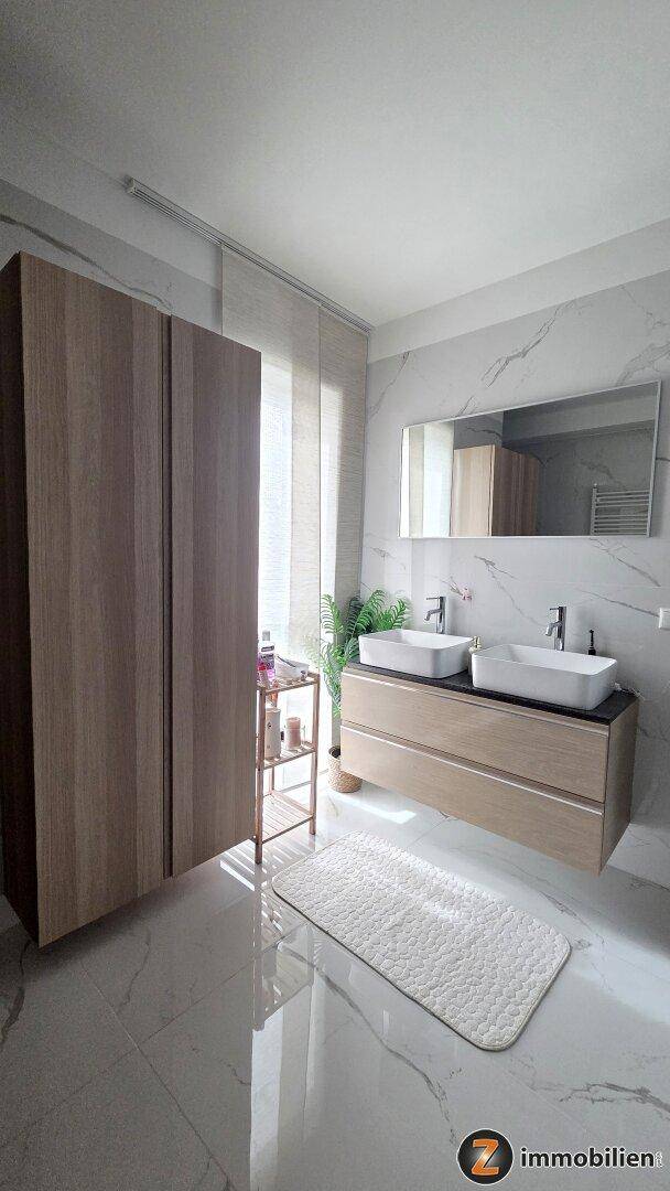 Modernes Badezimmer mit Doppelwaschbecken, großem Spiegel und eleganten Marmorfliesen.