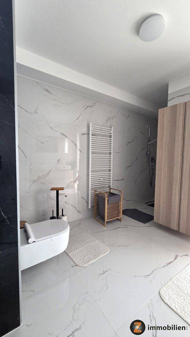 Modernes Badezimmer mit wandhängender Toilette, beheiztem Handtuchhalter und Marmoroptik-Fliesen.