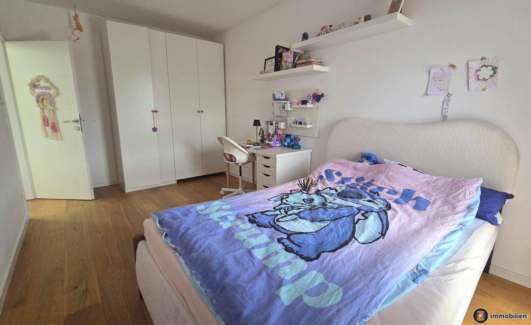 Helles Kinderzimmer mit Bett, weißem Kleiderschrank und einem Schreibtisch mit Regalen.