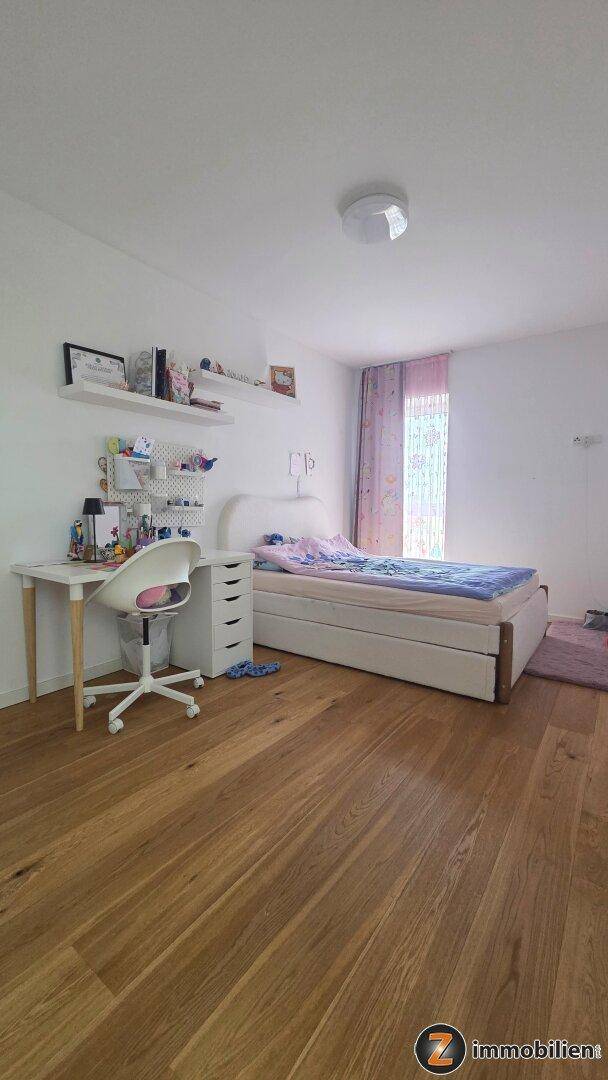 Geräumiges Kinderzimmer mit Holzboden, einem Bett und einem Schreibtisch am Fenster.
