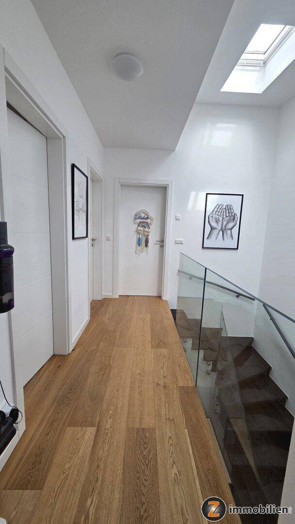Heller Flur im Obergeschoss mit Holzboden, Türen zu weiteren Räumen und einem Dachfenster.