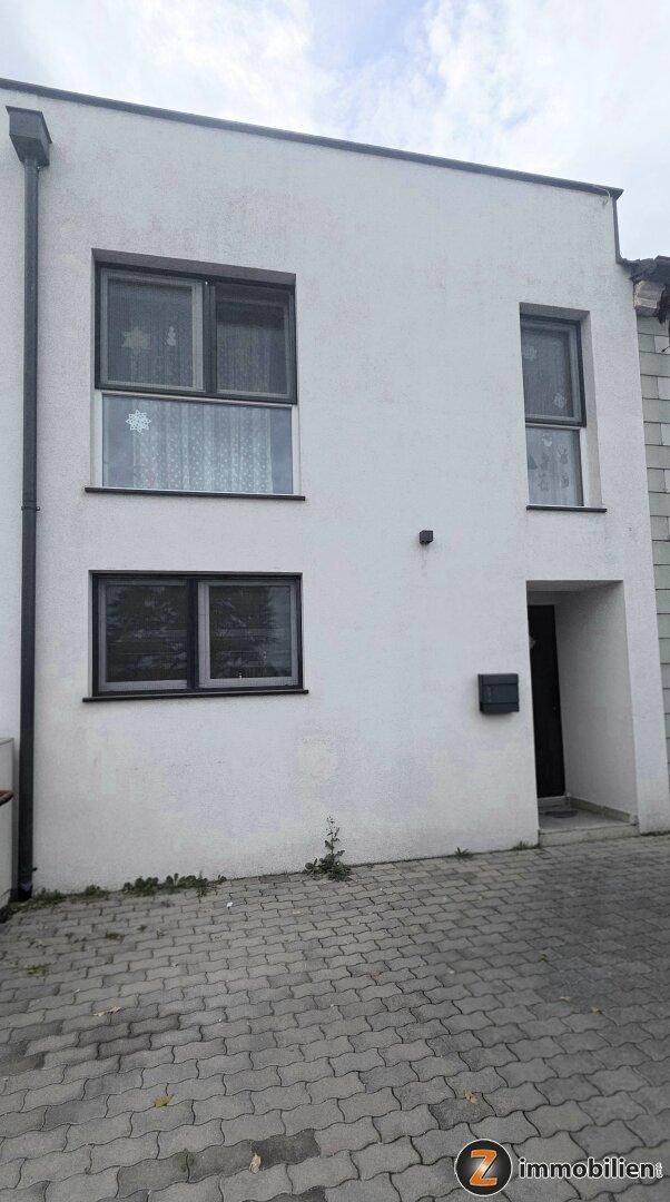 Moderne Hausfassade mit Eingangsbereich und gepflasterter Zufahrt.