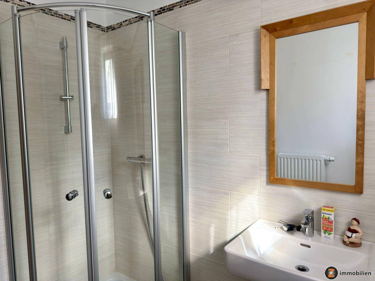 Modernes Badezimmer mit Duschkabine, Waschbecken und hellen Fliesen.