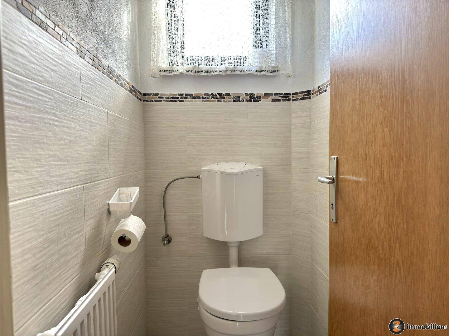 Separate Toilette mit Fenster, Wand-WC und hellen Fliesen.