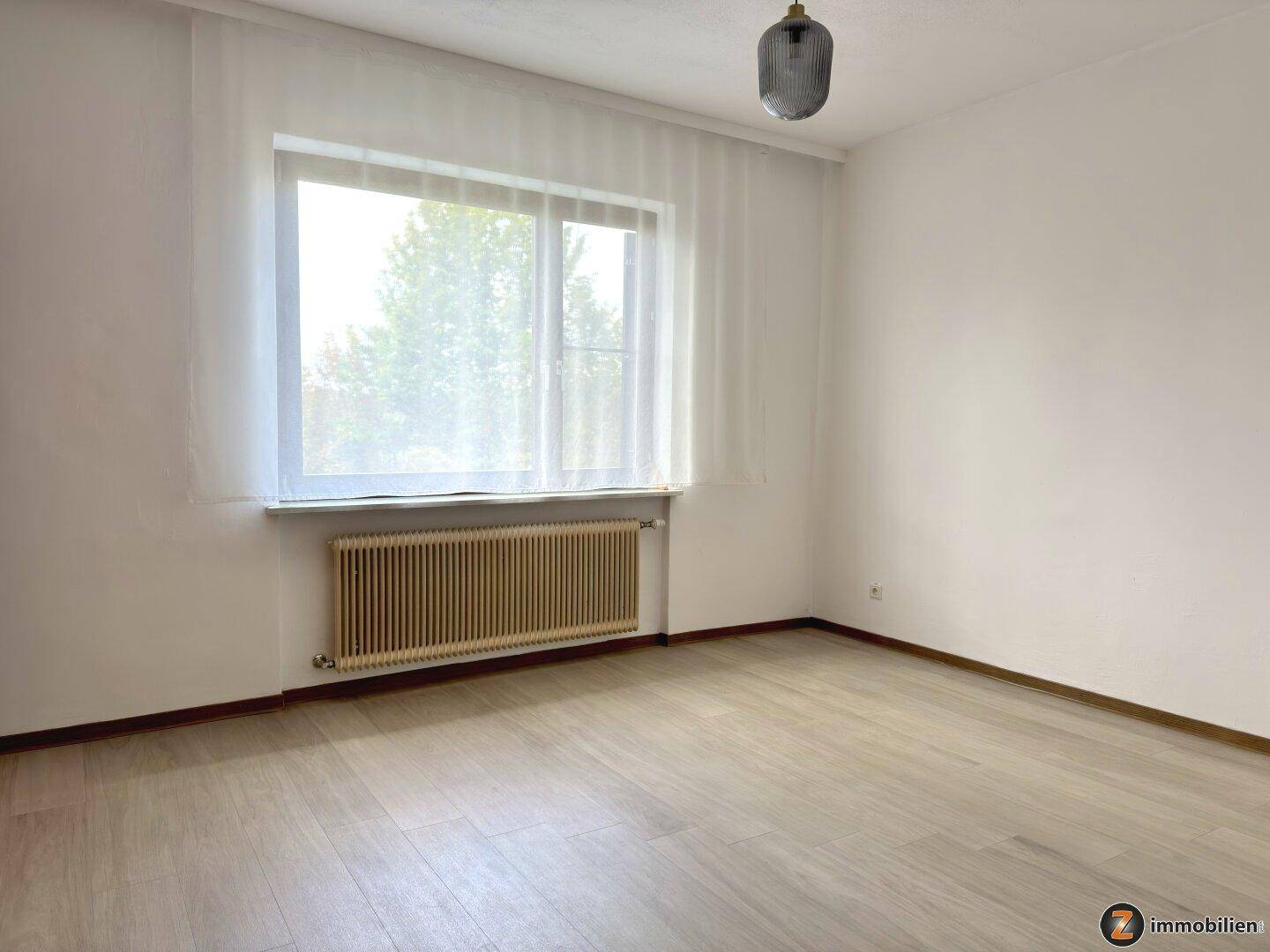 Helles Schlafzimmer mit Laminatboden und großem Fenster für viel Tageslicht.
