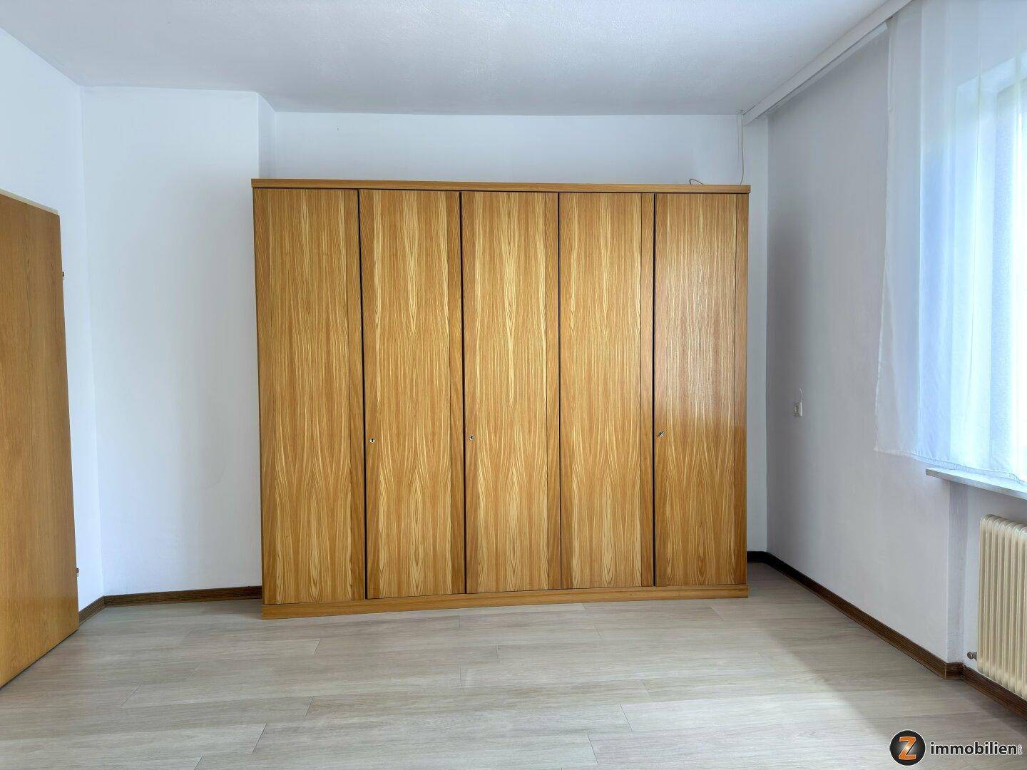 Schlafzimmer mit Laminatboden und großem Holzschrank für ausreichend Stauraum.