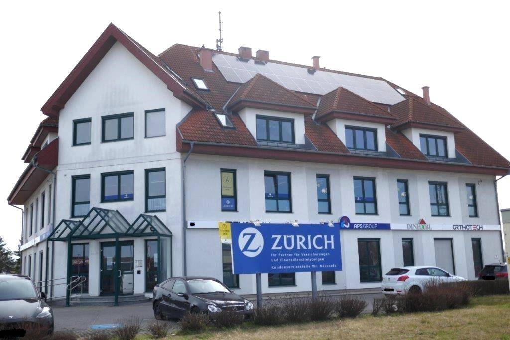 Mehrstöckiges Geschäftsgebäude mit weißer Fassade, rotem Ziegeldach und Solaranlage auf dem Dach.