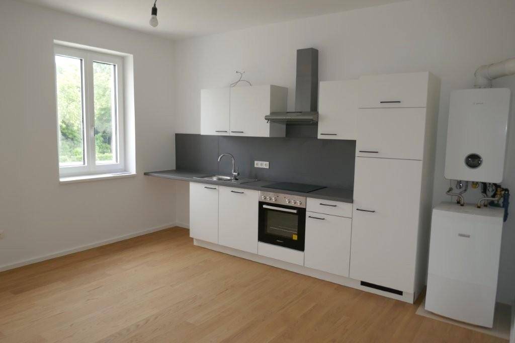 Moderne Einbauküche mit weißen Schränken, dunkler Arbeitsplatte und hellem Holzfußboden.