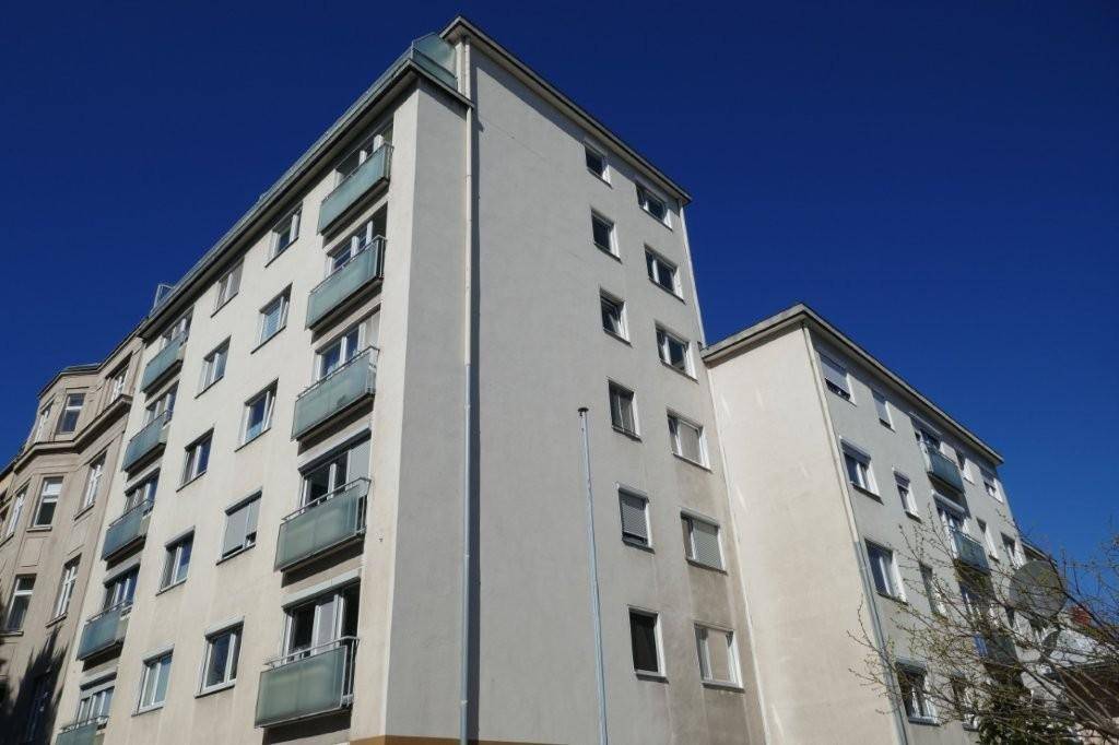 Mehrstöckiges Wohngebäude mit hellen Fassaden und Balkonen unter blauem Himmel.