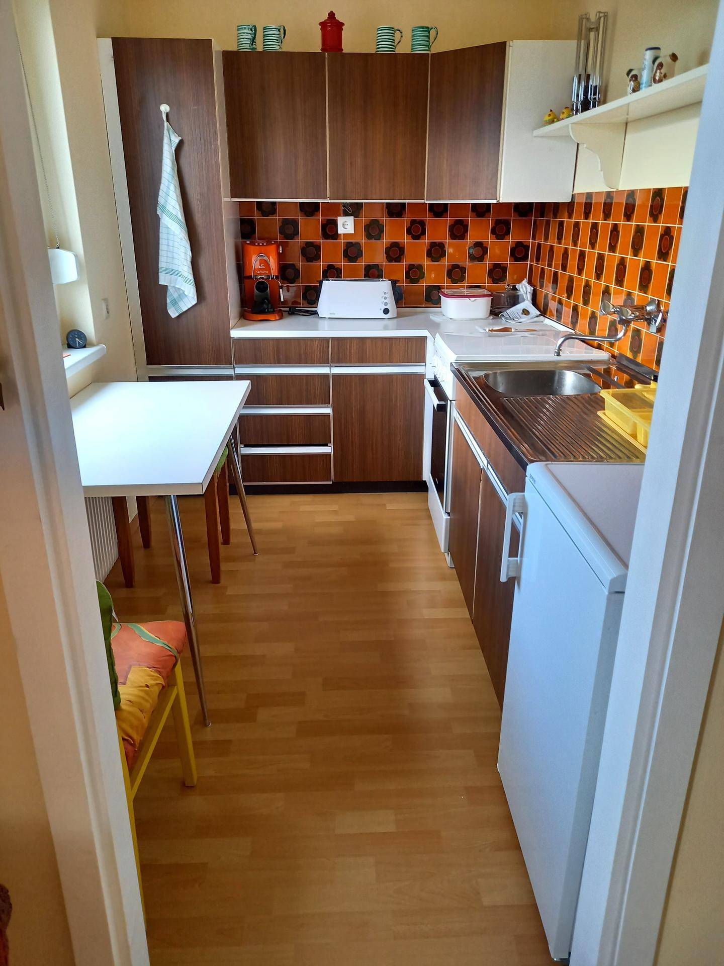 Kleine Küche im Retro-Stil mit dunklen Holzschränken, orangefarbenen Fliesen und Essbereich.