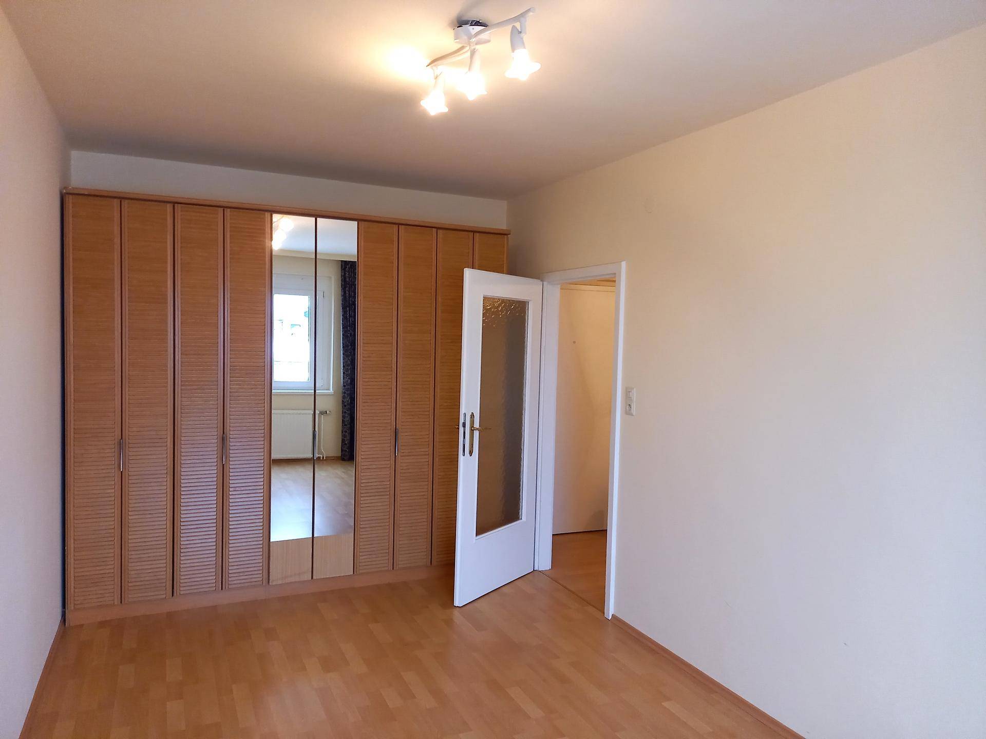 Schlafzimmer mit Laminatboden und einem großen Kleiderschrank mit Spiegeltüren.
