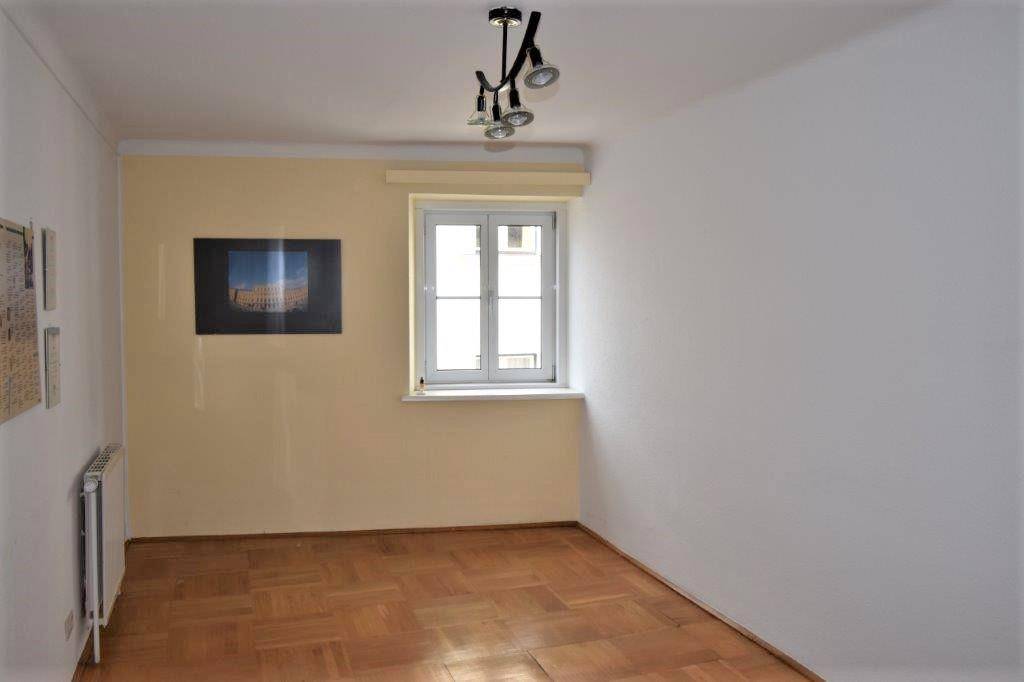 Heller Raum mit Parkettboden, einem Fenster und einer modernen Deckenleuchte, teilweise mit beigen Wänden.