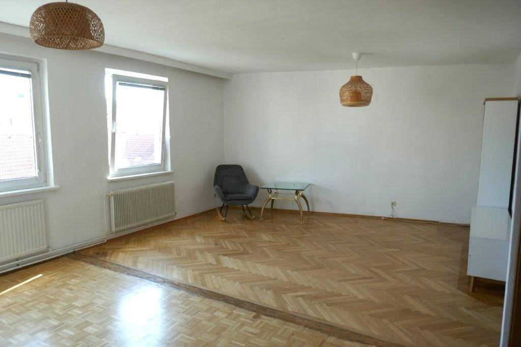 Helles Wohnzimmer mit Fischgrätparkettboden, großen Fenstern und zwei modernen Hängelampen.