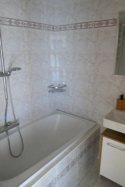 Badezimmer mit Badewanne, Duschfunktion, Waschbecken und hellen Fliesen mit dekorativer Bordüre.