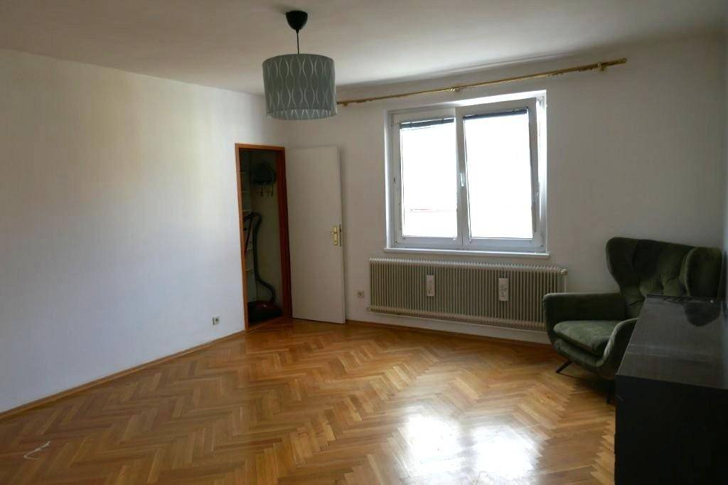 Geräumiges Zimmer mit Fischgrätparkett, einem großen Fenster und einem kleinen Abstellbereich.