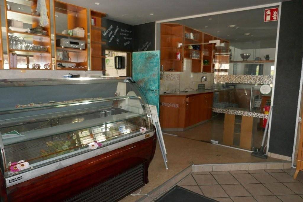 Kommerzielle Küche und Thekenbereich mit Holzregalen, Fliesenboden und Kühlvitrine.