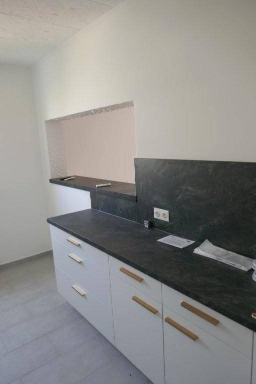 Teilansicht einer modernen Küche mit dunkler Arbeitsplatte und einer praktischen Durchreiche zur Wand.