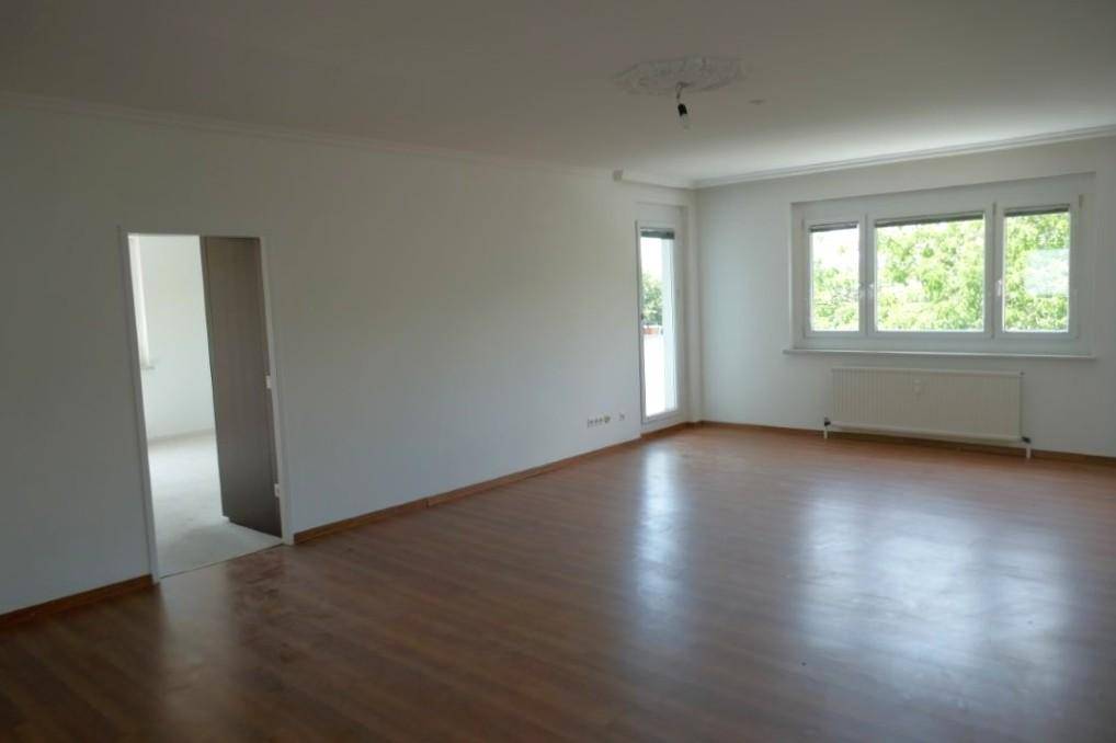 Heller Wohnbereich mit Laminatboden, weiß gestrichenen Wänden und Zugang zu einem weiteren Zimmer.
