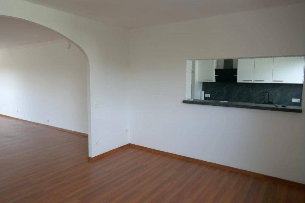 Offener Wohnbereich mit Laminatboden und einer praktischen Durchreiche zur angrenzenden Küche.