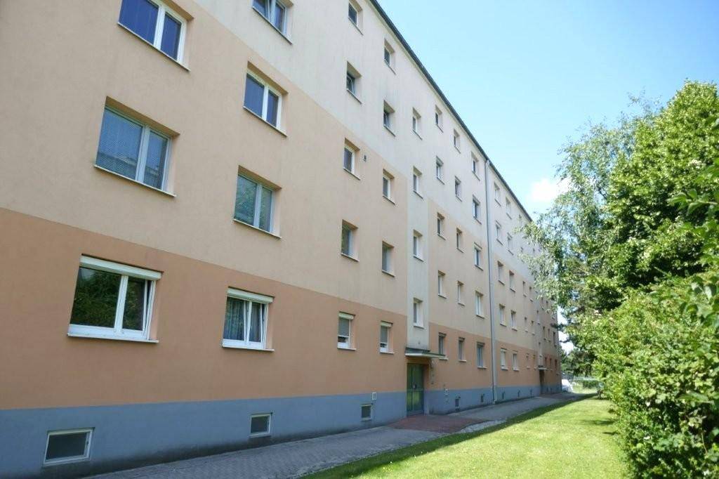 Seitenansicht eines gepflegten Mehrfamilienhauses mit beiger und grauer Fassade sowie zahlreichen Fenstern.