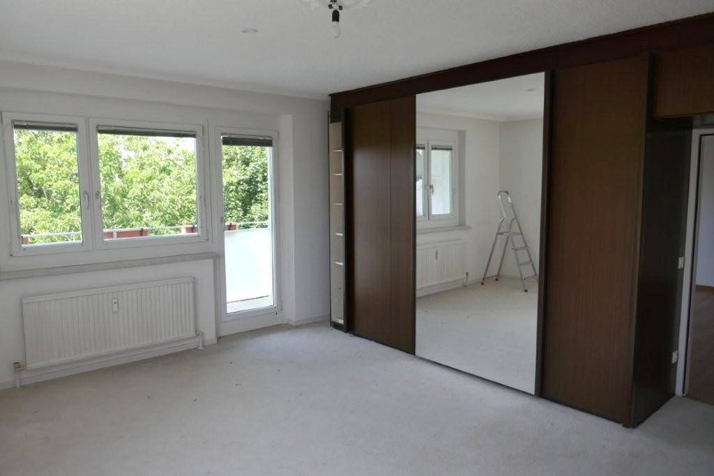 Schlafzimmer mit großem Spiegelschrank, breiter Fensterfront und direktem Zugang zu einem Balkon.
