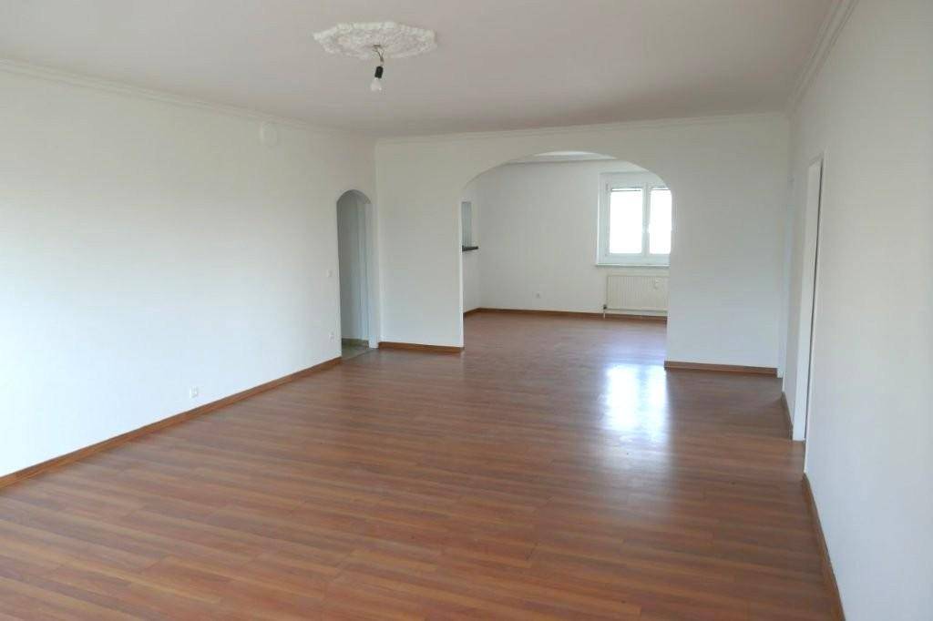 Helles, unmöbliertes Wohnzimmer mit Laminatboden, weiß gestrichenen Wänden und dekorativer Deckenrosette.