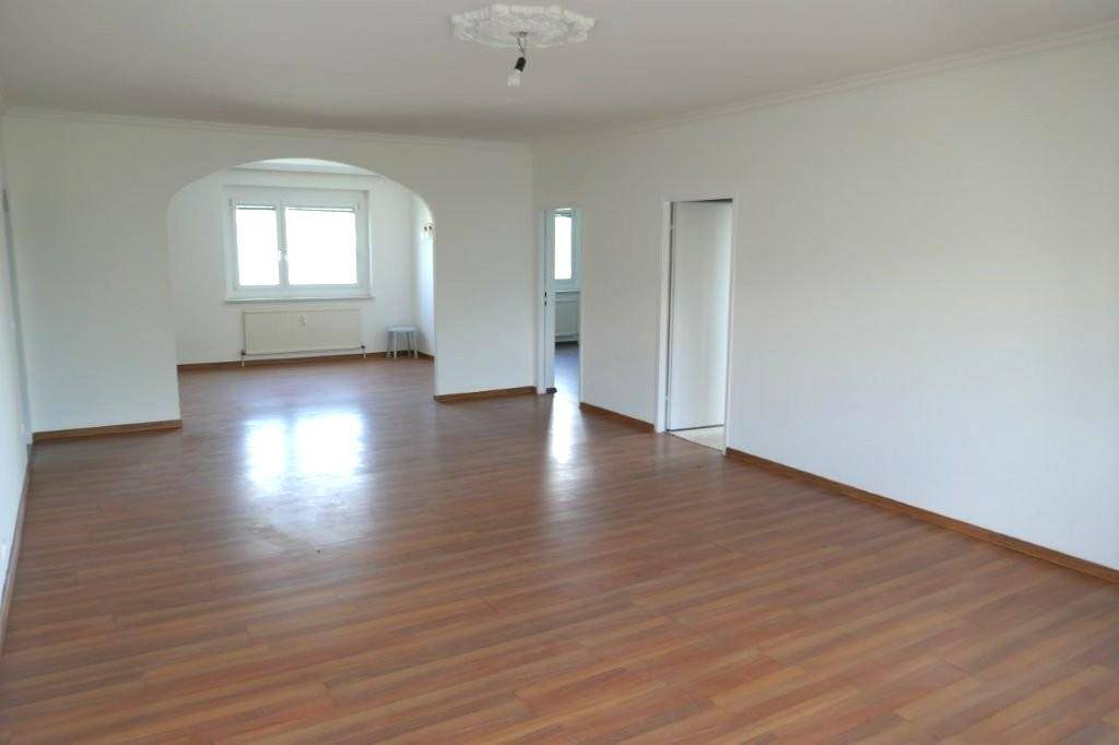 Geräumiges Wohnzimmer mit Laminatboden, weißer Decke und einem eleganten Bogen zu einem angrenzenden Raum.