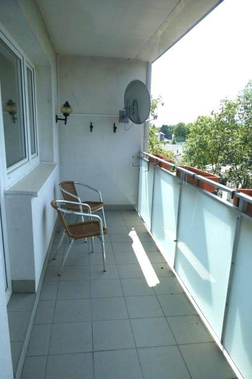 Sonniger Balkon mit Fliesenboden, transparenter Glasbrüstung und zwei gemütlichen Stühlen.
