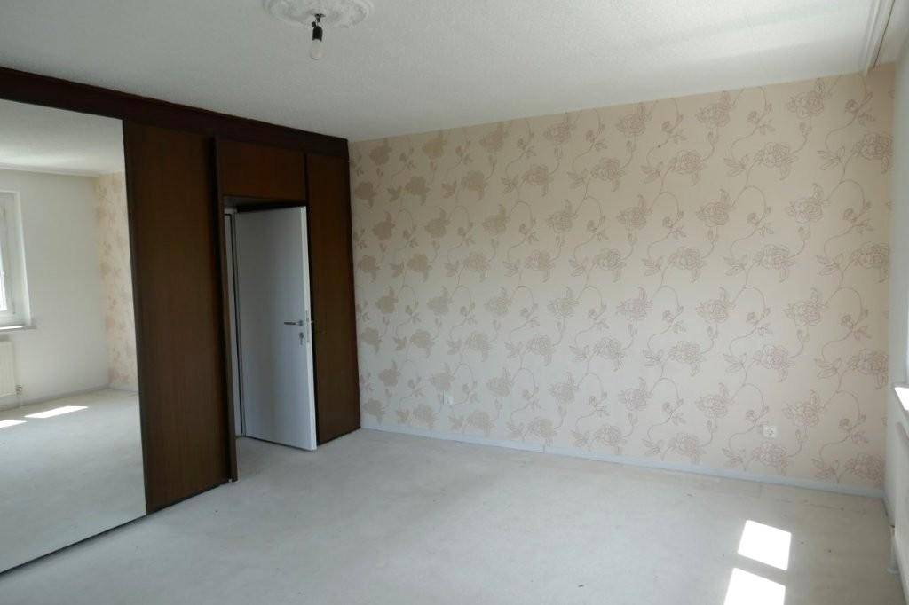 Schlafzimmer mit auffälliger floraler Tapete, Spiegelschrank und hellem Teppichboden. Gut erhalten.