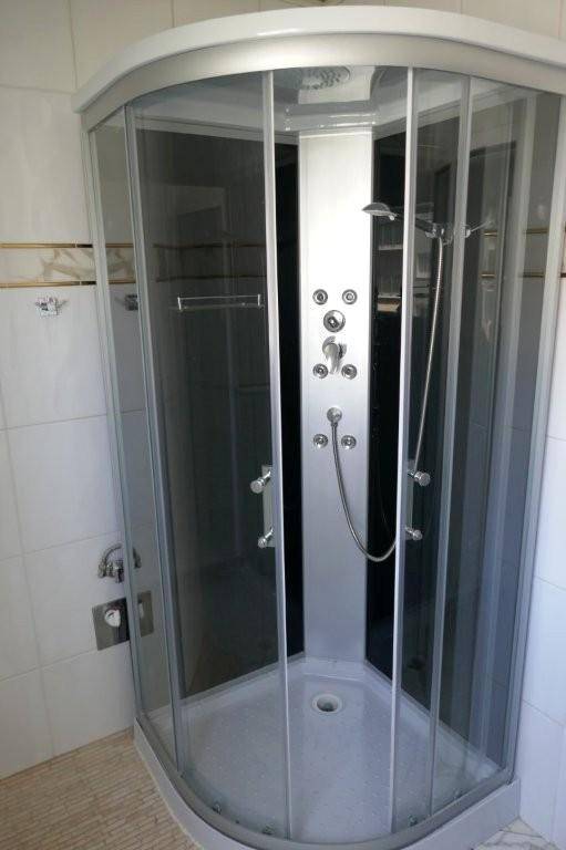 Modernisierte Duschkabine mit Glaswänden und integrierten Duschdüsen in einem gefliesten Badezimmer.