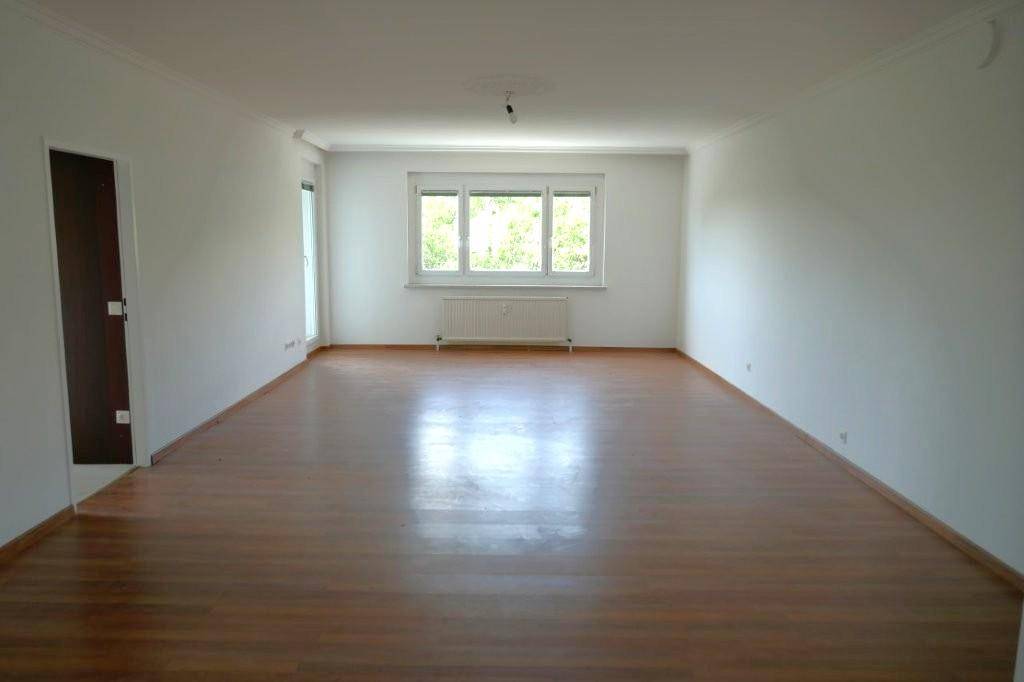 Großes, helles Wohnzimmer mit Laminatboden, weißen Wänden und einer breiten Fensterfront für viel Licht.